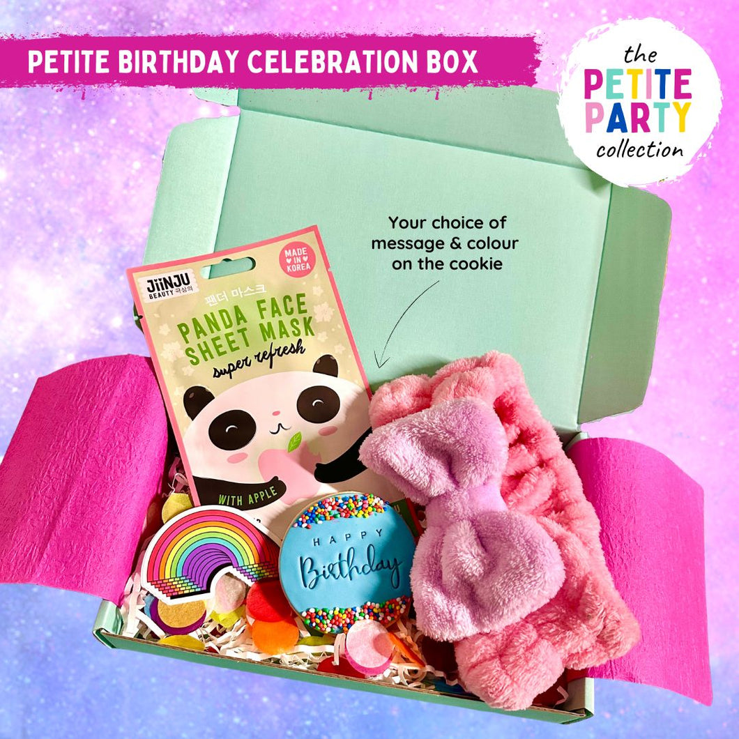 A small gift box floating on a sparkly pink and purple background with a sheet face mask, fluffy headband, handmade happy birthday cookie with blue icing and a rainbow sticker.