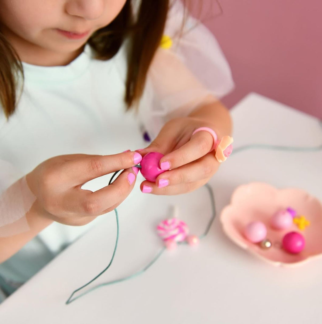 little girl beading a necklace with pink beads